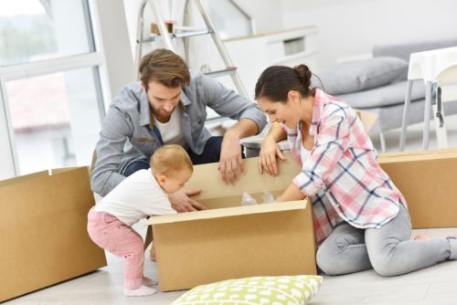 man and woman opening moving box with baby