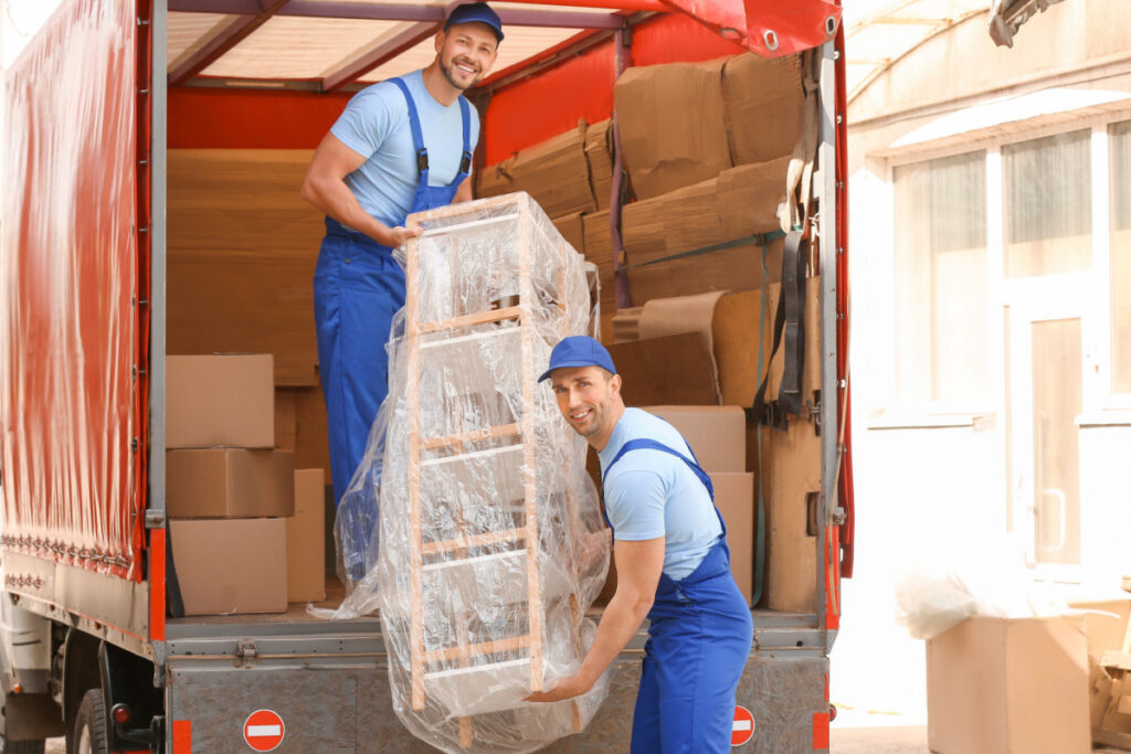 Two smiling movers transporting furniture out of a moving truck.