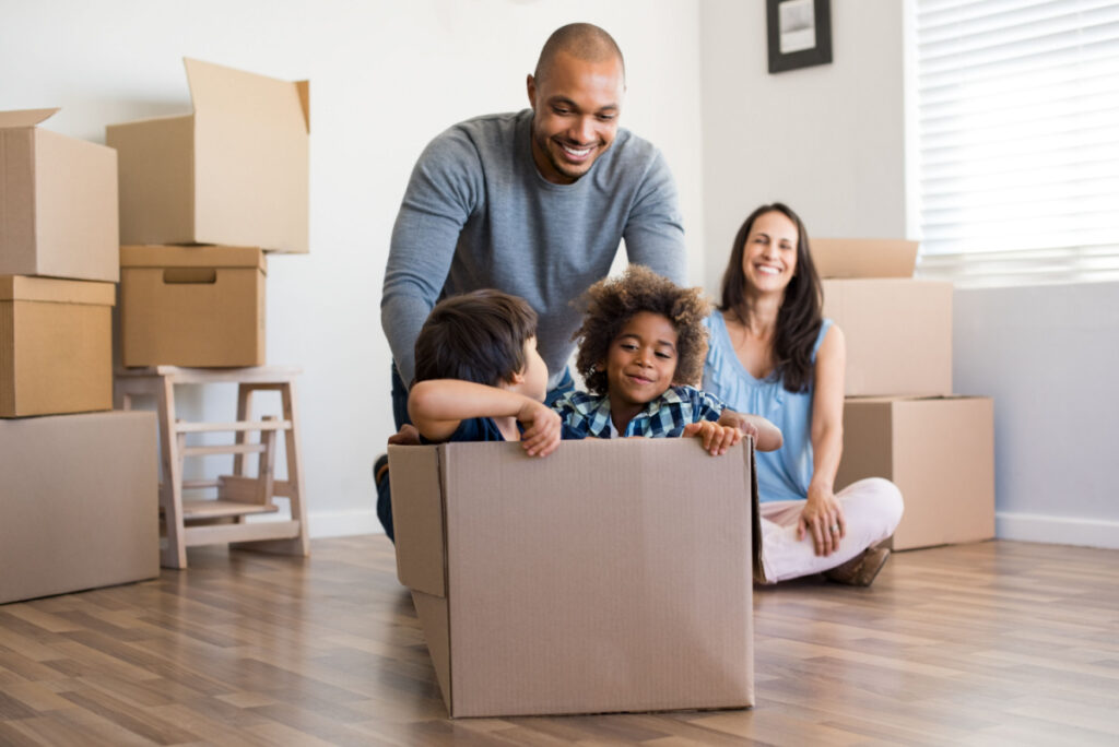 A family gathered around stacks of cardboard moving boxes.